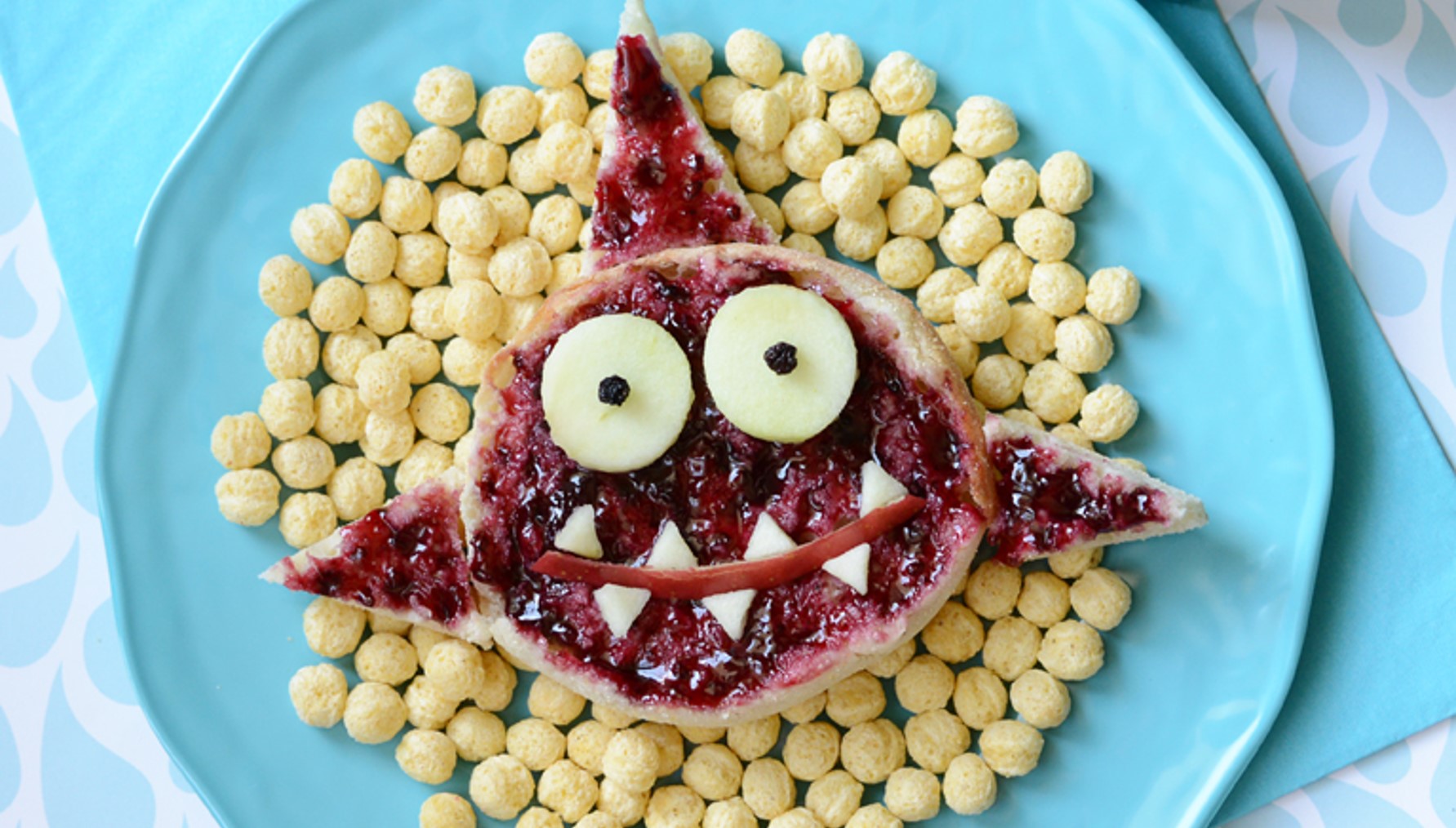 Kix cereal pieces on a blue plate with a jelly toast  shaped like a friendly shark on top of them